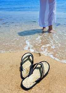 海滩拖鞋上沙子和女性的脚在海边缘