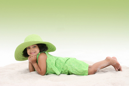 年轻美丽的女孩躺在沙子里穿的大顶绿色的帽子