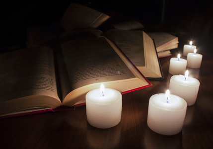打开书籍和黑暗的木桌上的蜡烛