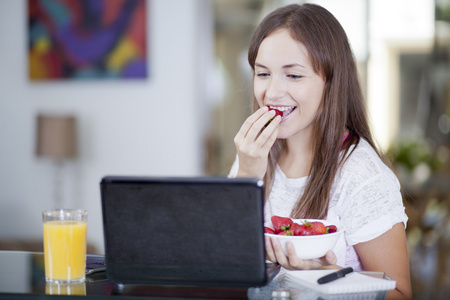 有草莓的同时使用一台笔记本电脑桌的女人，一杯果汁是桌子上