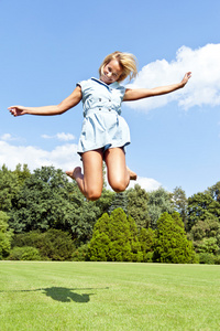 美丽的年轻女子跳上天空在公园在蓝色的裙子
