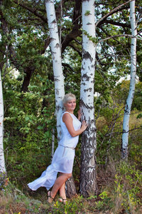 在夏季森林中白色长礼服的金发女郎