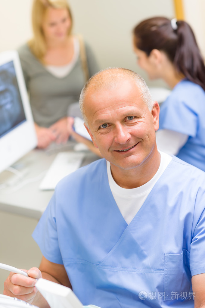 成熟的牙科医生在办公室与助理