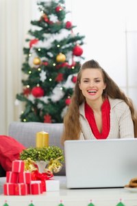 微笑着的年轻女子，发送电子邮件问候语的圣诞节树附近