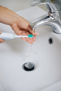 teethcare手在水流下清洗电动牙刷上特写照片