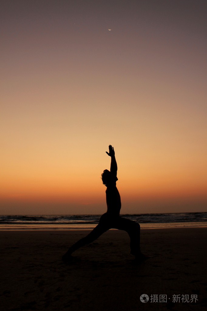 在日落的海边背景上的瑜伽姿势的男人剪影.月光下的战士