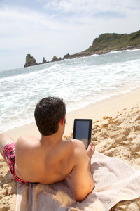 男子在海滩上使用电子平板电脑