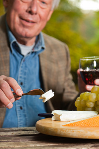 高级人类享受葡萄和奶酪户外在秋天的森林