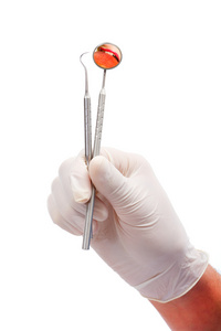 牙医手与橡胶防护手套持有牙科工具 一个探针和口腔的镜子，反映了一个女人的牙齿咬红的苹果上白色孤立