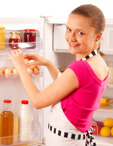 一个年轻女子使用冰箱里掏出鸡蛋。食品 牛奶 红酒和果汁在背景中