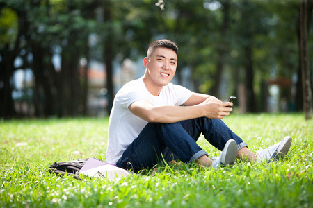 亚洲英俊学生打开一本书和微笑在户外