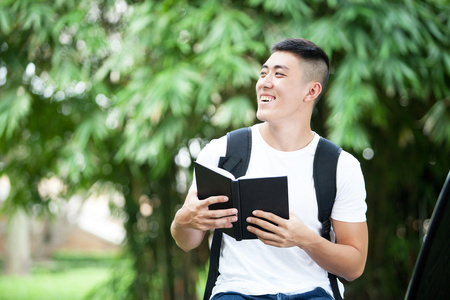 亚洲英俊学生打开一本书和微笑在户外