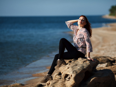 漂亮女孩坐在一块岩石由海