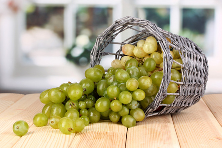 成熟的绿色葡萄在窗口背景上的木桌上的篮子里