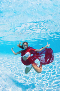 在游泳池中的红色面纱的水下女人时尚人像