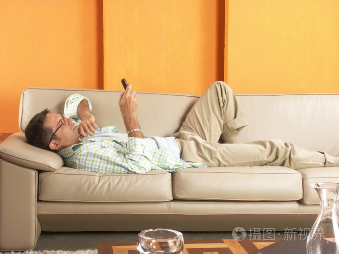 躺在沙发,手机上轻松年轻男子照片-正版商用图片1ajze7-摄图新视界
