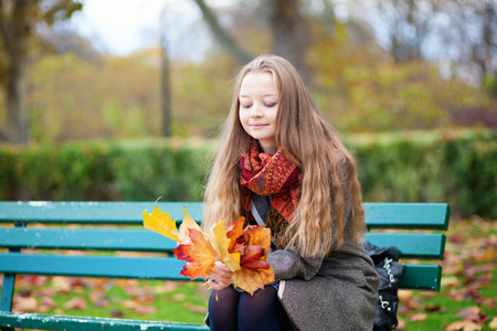 年轻美丽的女孩坐在长椅上了秋天的叶子在