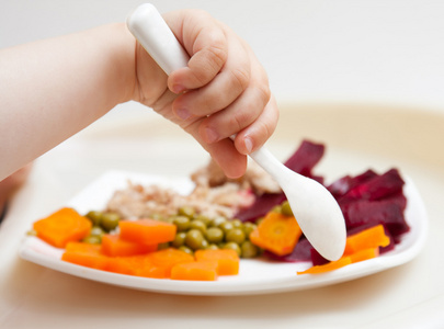 宝宝的手和一把汤勺板与蔬菜