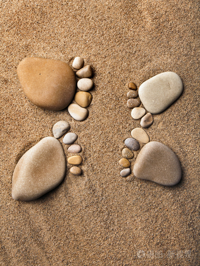 跟踪赤裸的双脚石头做的卵石海滩沙子的背景上