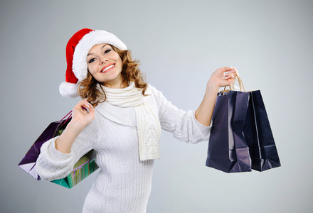 美丽的年轻女孩在购物袋的圣诞老人帽子