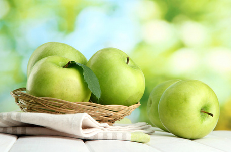 成熟的绿色苹果用叶子在篮子里，木桌上，在绿色背景上