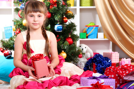 漂亮的小女孩身着节日的盛装与欢乐地装饰的屋子在他们手中的礼物