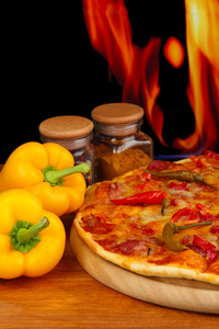 与火焰背景上的木制板上蔬菜美味意大利辣香肠比萨饼