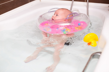 初生婴儿游泳的一间浴室和游泳在脖子上。童年和健康的概念