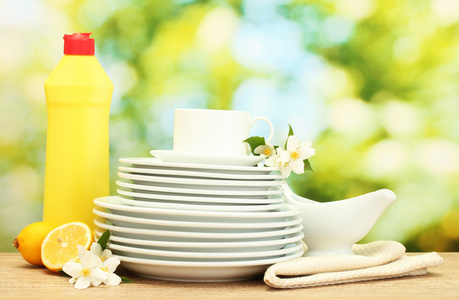 空干净盘子和杯子与洗洁精 鲜花和绿色背景上的木桌上的柠檬
