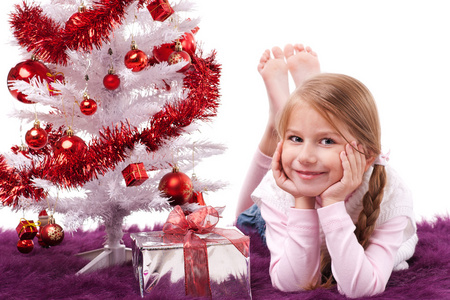女孩躺在白色的人造圣诞树边的地毯上，礼品