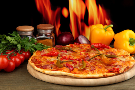 与火焰背景上的木制板上蔬菜美味意大利辣香肠比萨饼