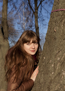 年轻的女孩，黑头发，棕色外套站在附近一棵树