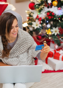 微笑与便携式计算机和信用卡圣诞节树附近的女人