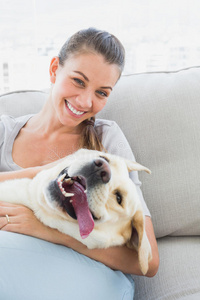 快乐的女人在沙发上搂着她的黄色拉布拉多犬