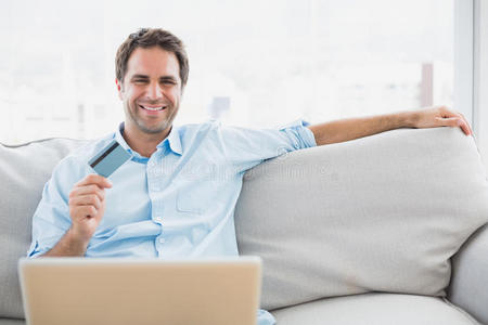快乐男人坐在沙发上用笔记本电脑购物