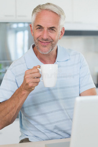 微笑的男人一边喝咖啡一边用笔记本电脑