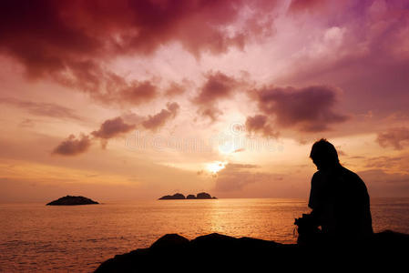 一个人坐在一块小岩石上看美丽的日出情侣相拥在海滩上的海边日出