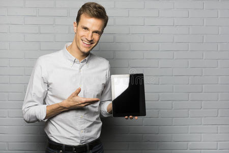 帅气微笑的男人展示着一台平板电脑，被隔离在灰色的b上