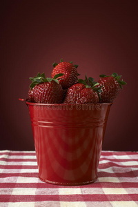 新鲜的红草莓放在一个红色的碗里，放在方格桌布上
