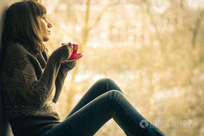 美丽的女孩在窗边喝咖啡做梦