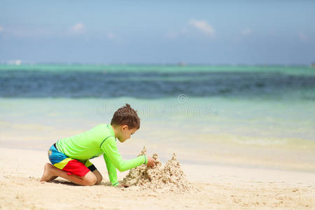 高加索男孩在热带海滩上建造沙堡