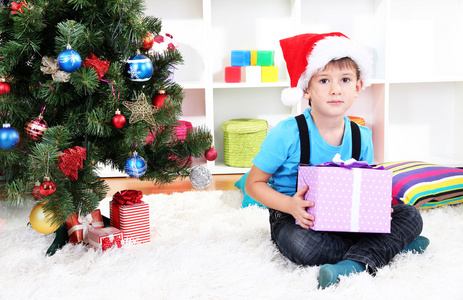 圣诞老人帽子的孩子坐在附近的圣诞树与手中的礼物