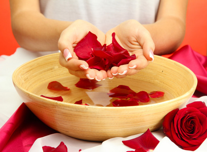 女人手用木碗水的花瓣，红色的背景上