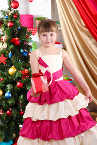 漂亮的小女孩身着节日的盛装与欢乐地装饰的屋子在他们手中的礼物