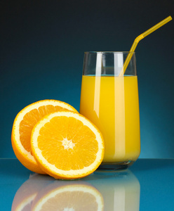 美味的橙汁在玻璃和它旁边暗蓝色背景上的橘子
