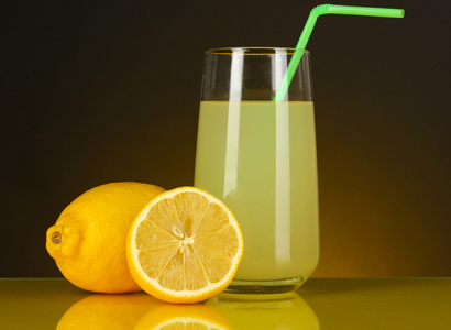 在玻璃和它旁边暗橙色背景上的柠檬美味柠檬汁