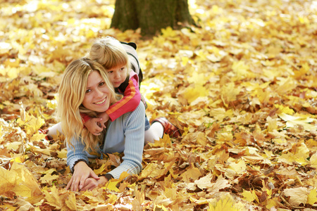 漂亮的小女孩和她的母亲在秋天的森林玩