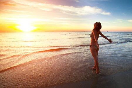 一个年轻的女人站在海滩上期间一个美丽的黄昏