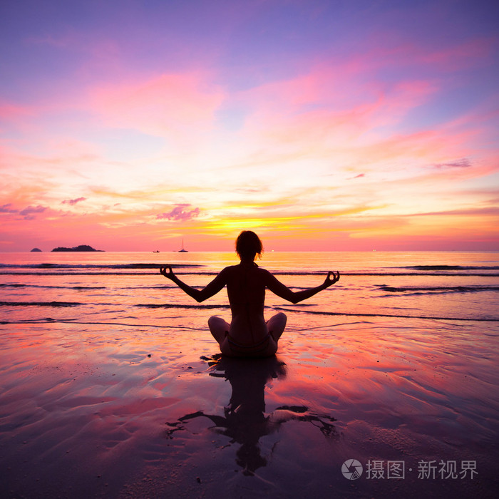 练瑜伽在夕阳西下的时候坐在沙滩上一个女人