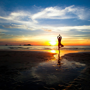 在一个美丽的黄昏期间练瑜伽在海滩上的女人的剪影